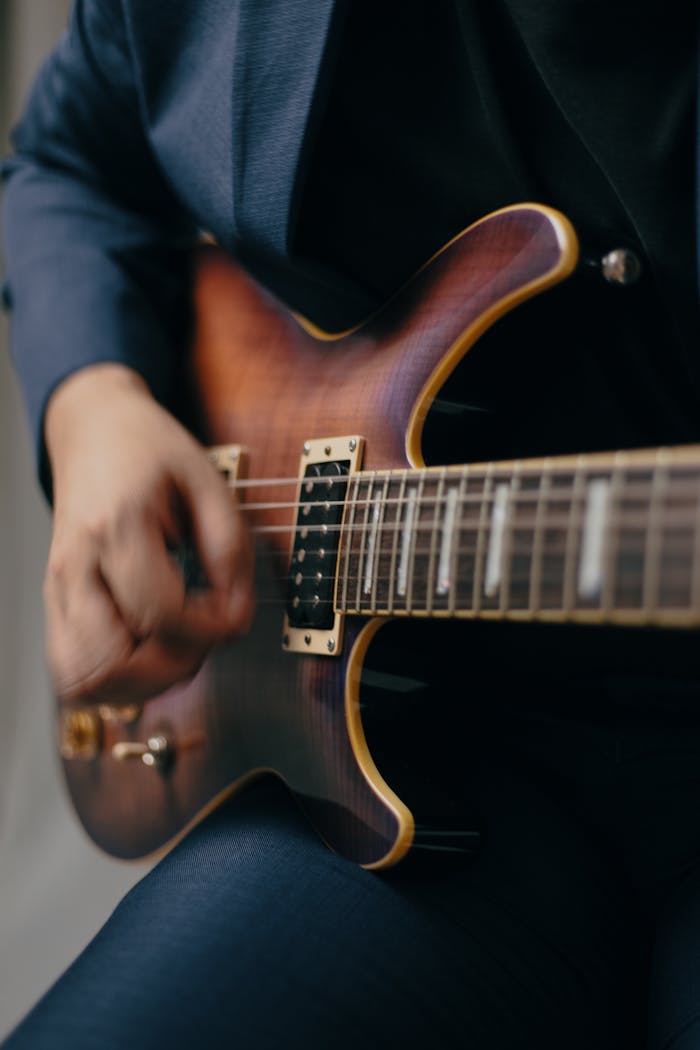 services-04 A man in a suit playing an electric guitar with focus on his hand strumming the strings.