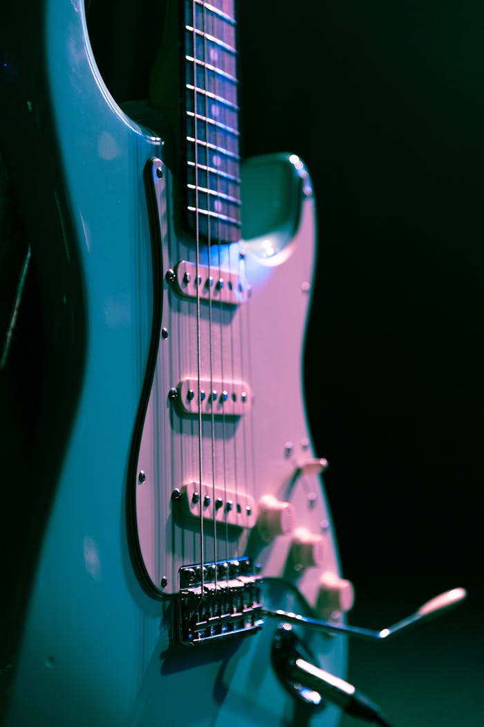 Detailed vertical shot of an electric guitar against a black background, highlighting its strings and design.