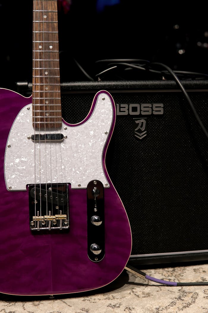 services-02 Close-up of a purple electric guitar next to a Boss amplifier.