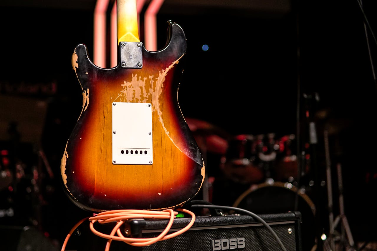 Close-up of a worn electric guitar with an amplifier on a dimly lit stage, creating a warm, vintage feel.