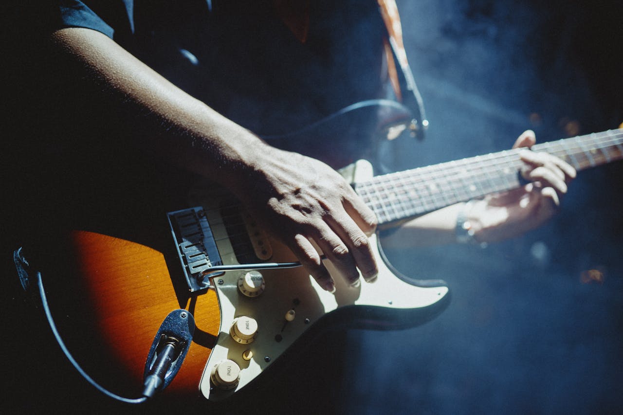 Close-up of a musician playing an electric guitar under stage lights, creating a vibrant atmosphere.