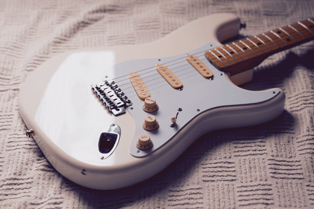 Closeup of a classic white Stratocaster electric guitar resting on textured fabric surface.
