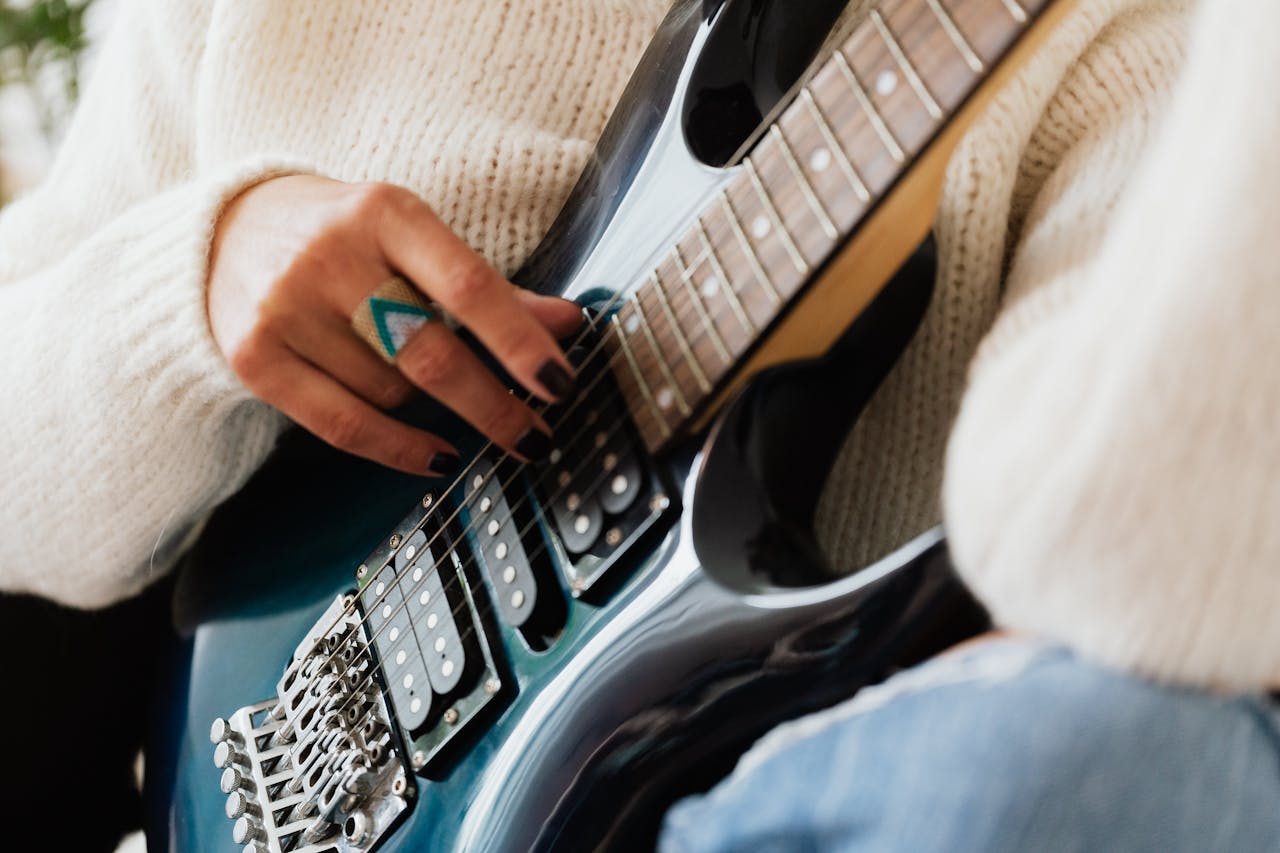 services-01 Crop faceless female guitarist with stylish ring wearing white sweater and jeans performing contemporary dark blue guitar